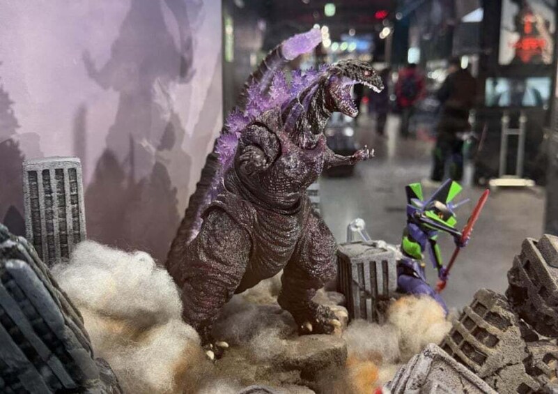 A model of Godzilla on a rocky terrain with a cityscape in the background. 3