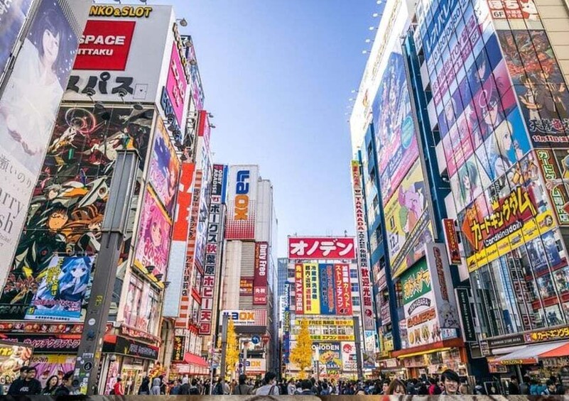 A bustling urban street with tall buildings adorned with colorful advertisements and signs. 1