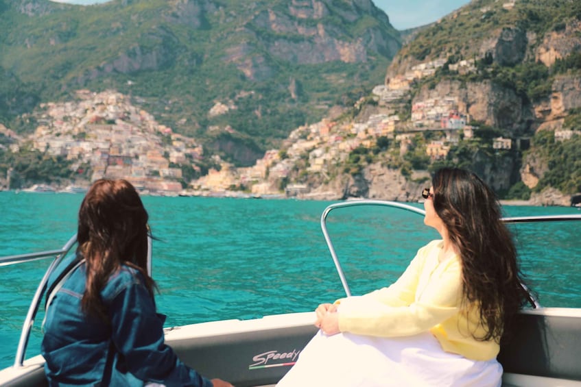 Two people on a boat with a coastal town and mountains in the background. 2