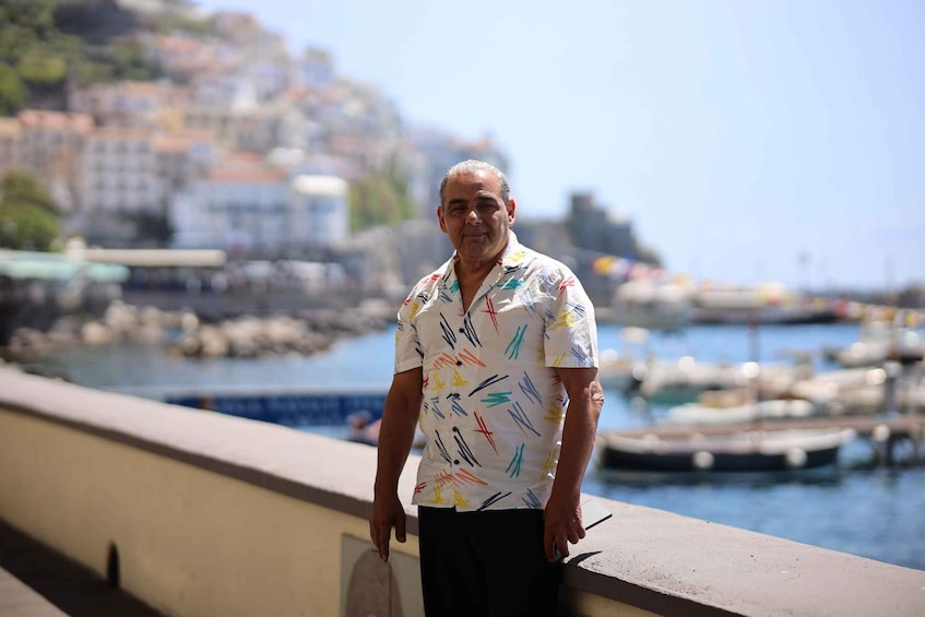 A man standing by a waterfront with boats and buildings in the background. 5