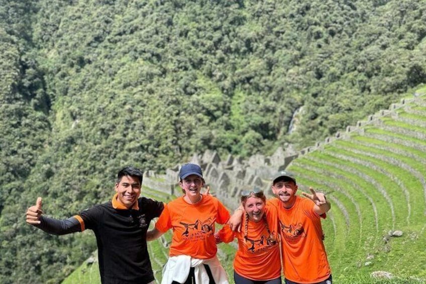 Three people in orange shirts standing on a hillside with terraced fields in the background. 1