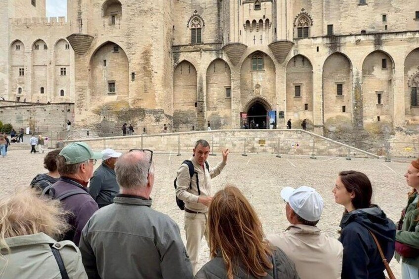 A group of people gathered in front of a historic building with arched windows and a central entrance. 1