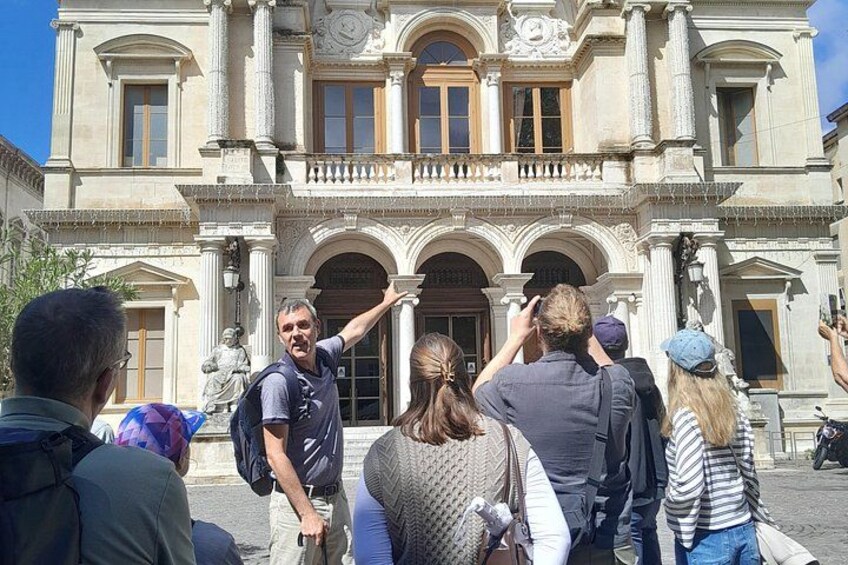A group of people standing in front of a historic building with columns and arched windows. 1