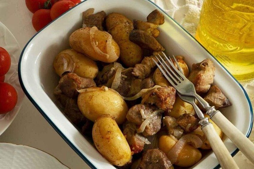 En skål med ristede kartofler og kød, en gaffel og et glas gul væske. 4