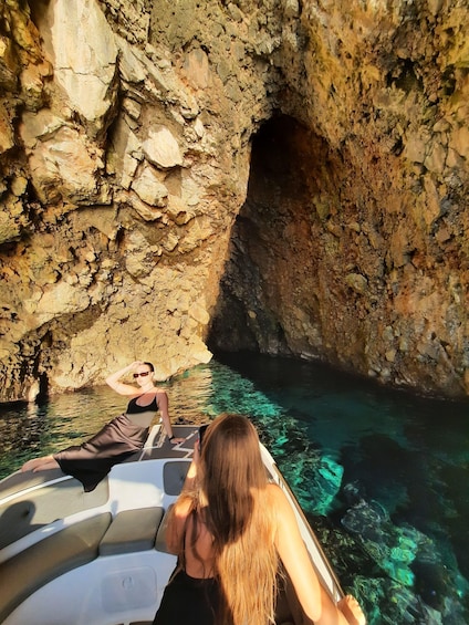 A boat with two people, one taking a photo, near a rocky cave entrance with clear water. 3