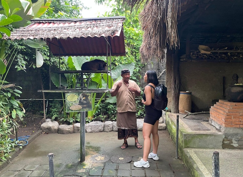 A man and a woman standing in a zoo enclosure with a large animal enclosure and a traditional structure in the background. 5