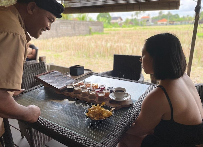 A man serving coffee to a woman at an outdoor table with a view of a rice field. 4