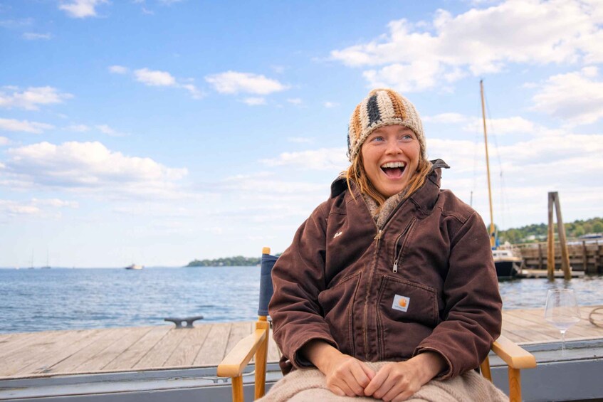 A person sitting on a wooden dock chair by a body of water with a clear sky. 1