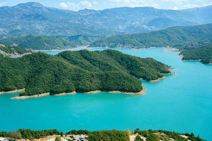 A turquoise lake surrounded by dense green forest and mountains. 5