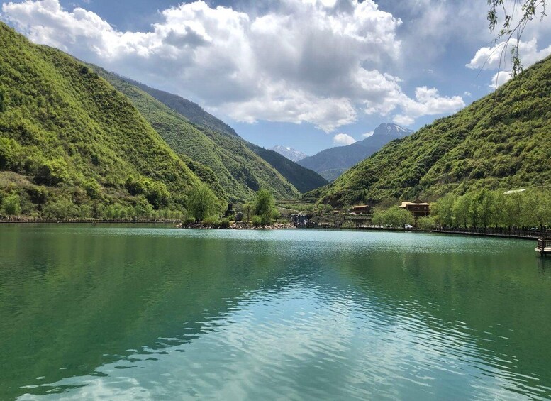 A serene lake surrounded by lush green hills and a mountain range in the background. 1