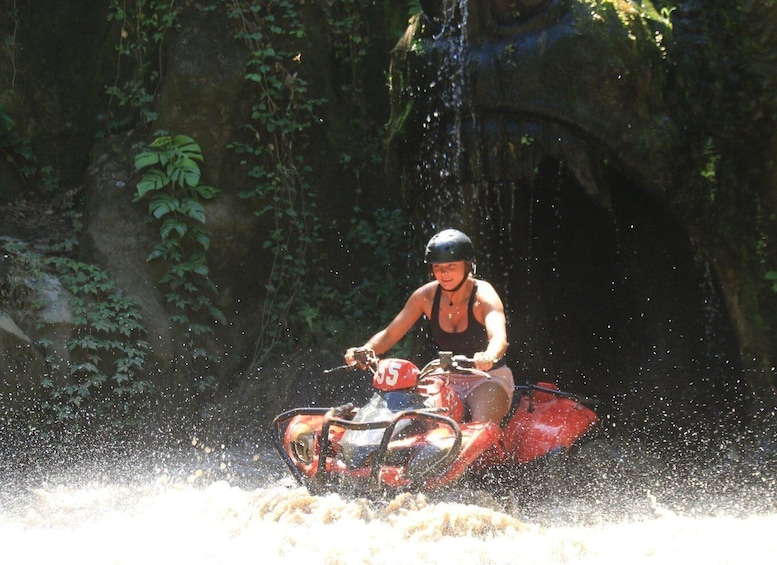 A person riding a red ATV through a water splash. 3