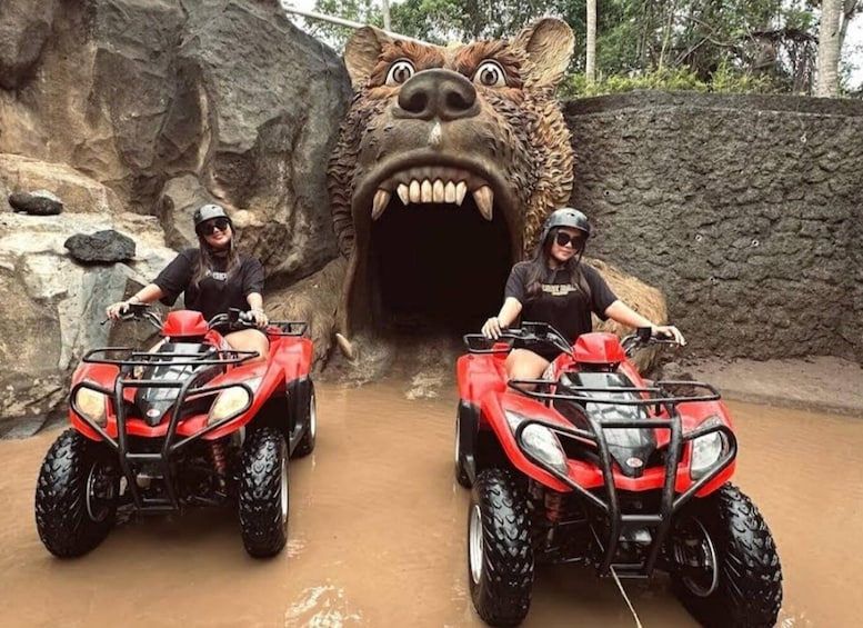 Two people on red ATVs approaching a rocky tunnel with a large, menacing animal head. 2