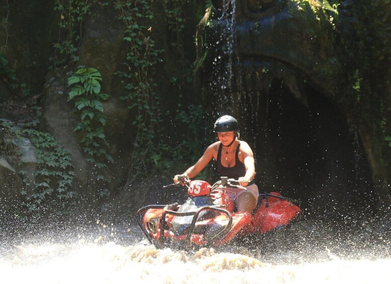 A person riding a red ATV on a water trail surrounded by dense foliage. 2