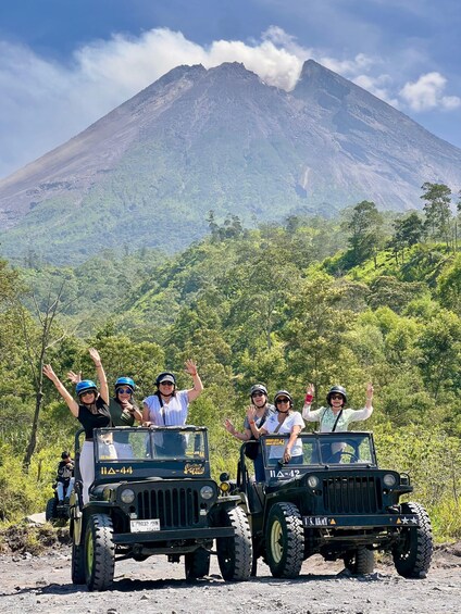 Two jeeps with passengers waving, a mountain, and a forested landscape. 2