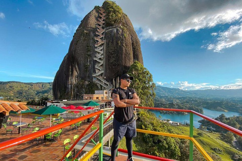 A person standing on a platform with a large rock formation in the background. 1
