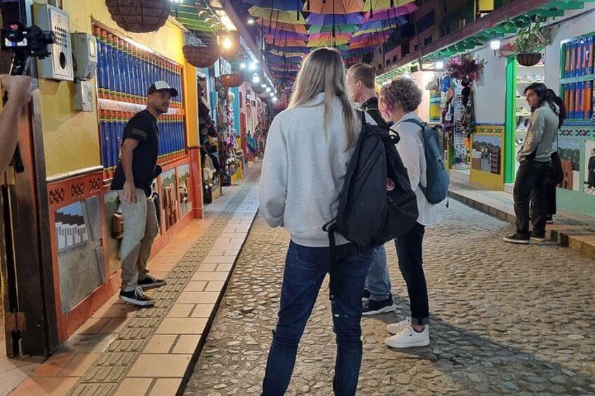 A cobblestone street lined with colorful shops and a person standing by a display. 5
