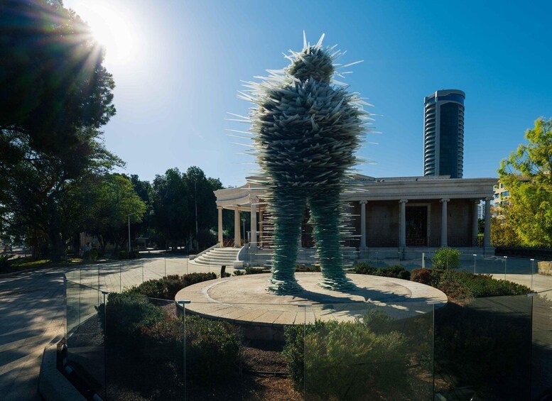 A tall, spiky sculpture in a circular plaza with a building in the background. 3