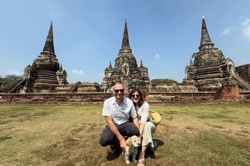 A man and a woman sitting on grass with ancient temple ruins in the background. 3