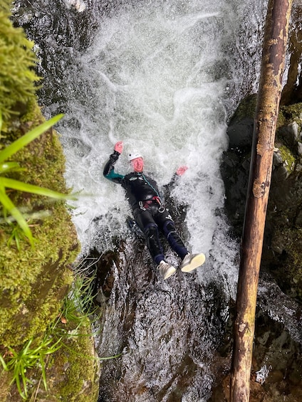 A person in a wetsuit and helmet, lying on a rock in a turbulent water flow. 2