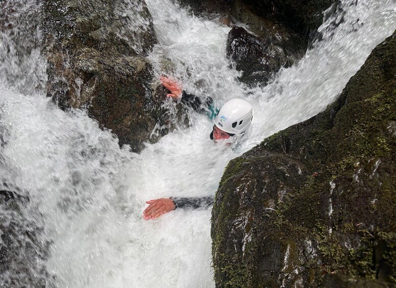 A person in a white helmet and red jacket navigating a turbulent river with strong currents and rocky obstacles. 3