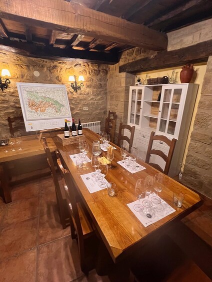 A rustic dining room with a wooden table set for a meal, stone walls, and a map on the wall. 2