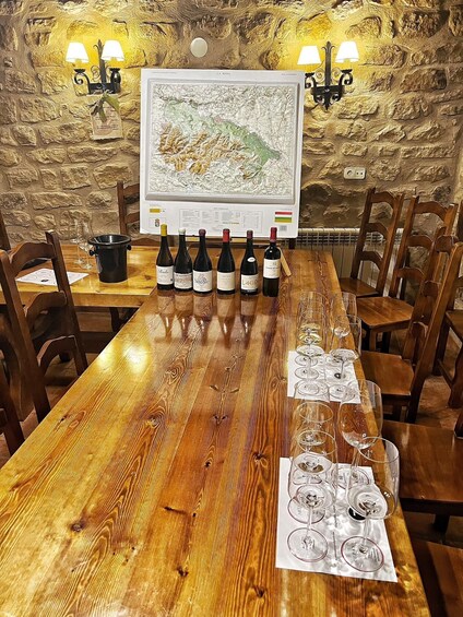 A wooden table with wine bottles and glasses, a map, and stone wall decor. 1