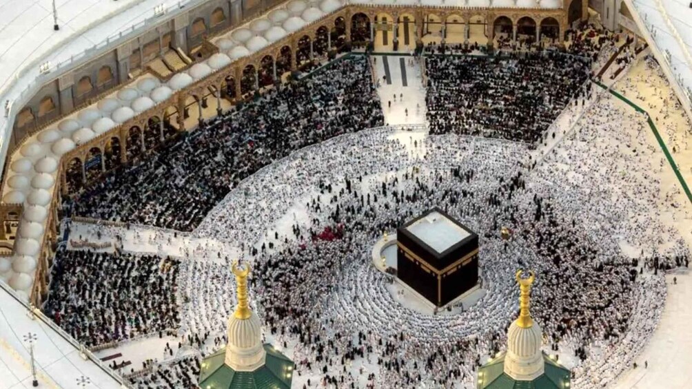 A large, circular structure with a central black cube, surrounded by a crowd. 1