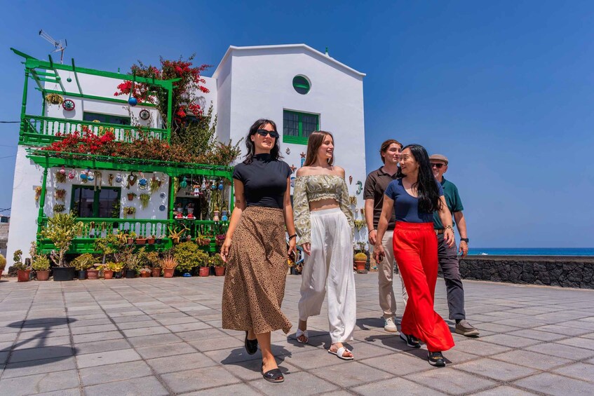 A group of people walking on a paved area with a white building and green balconies adorned with plants and flowers. 1