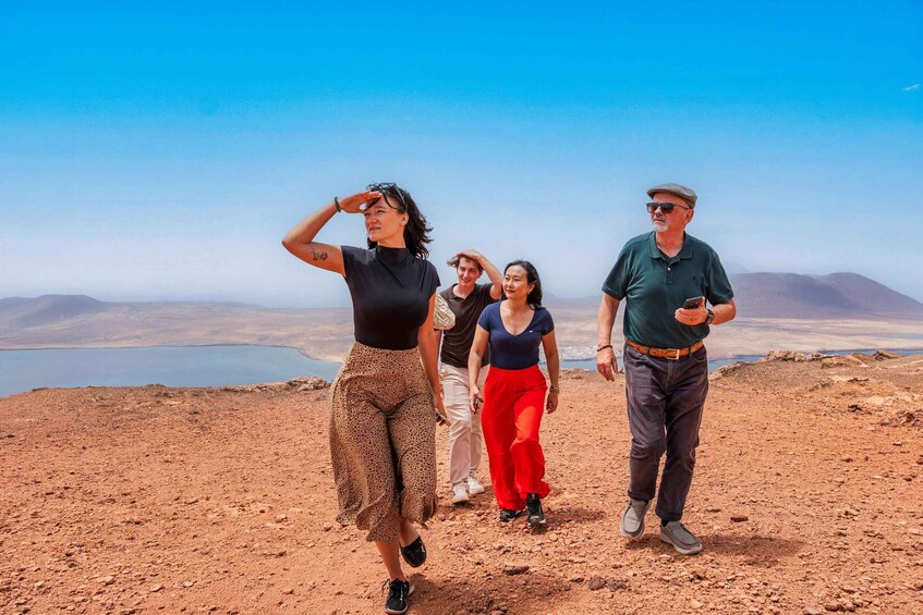A group of people walking on a rocky terrain with a lake and mountains in the background. 3