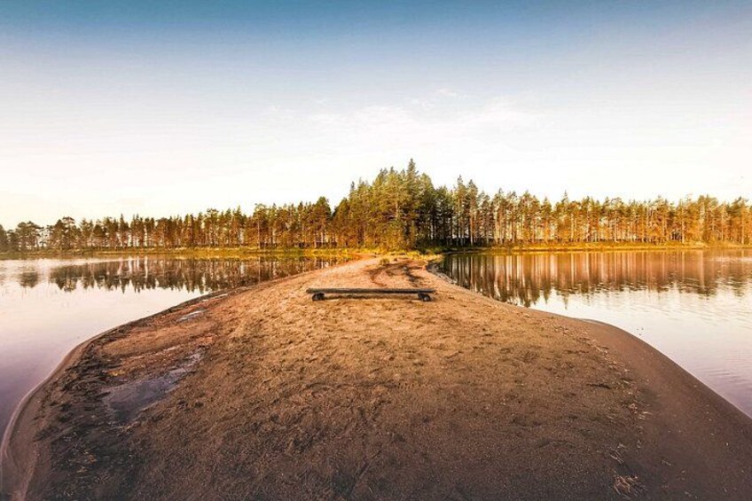 A calm lake with a sandy beach and a bench. 3