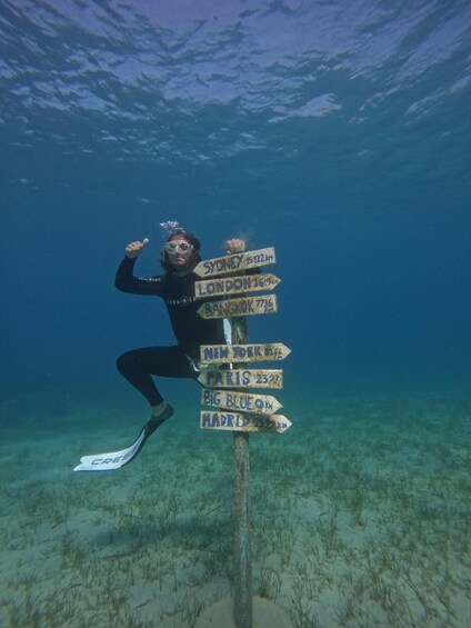 A diver underwater holding a signpost with city names and distances. 2