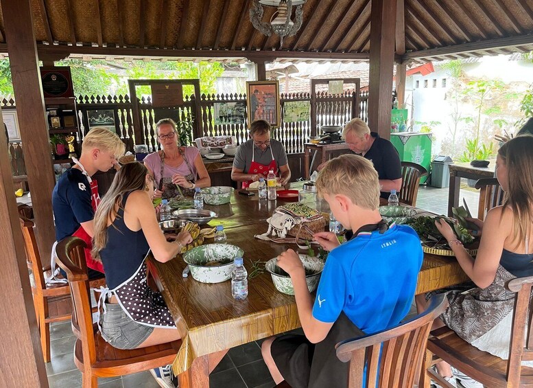 A group of people seated around a wooden table at an outdoor cafe, engaged in conversation and food preparation. 2