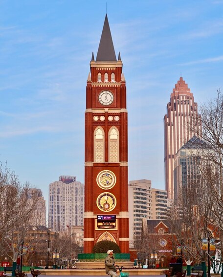 A tall clock tower with a pointed roof, surrounded by modern buildings and leafless trees. 2