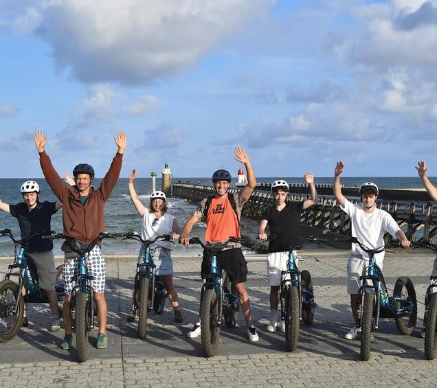 A group of people on bicycles by the seaside, with a lighthouse in the background. 2