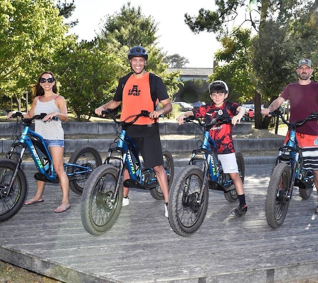 Four people on bicycles in an outdoor setting with trees and a paved area. 4