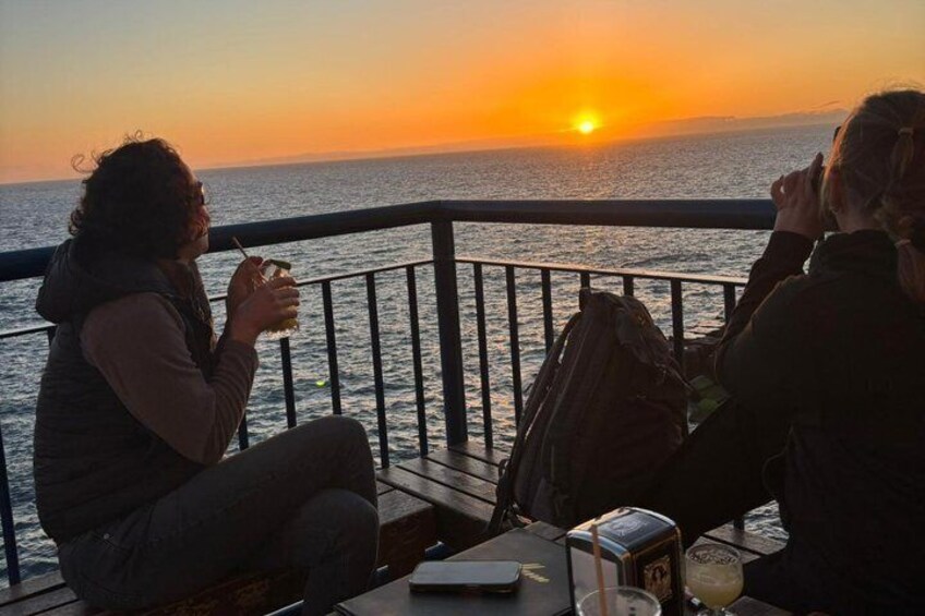 Two people sitting by a railing, overlooking a sunset over the ocean. 3
