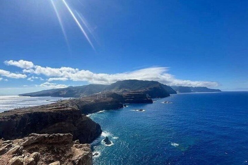 A coastal landscape with cliffs, a clear blue sea, and distant mountains under a sunny sky. 1