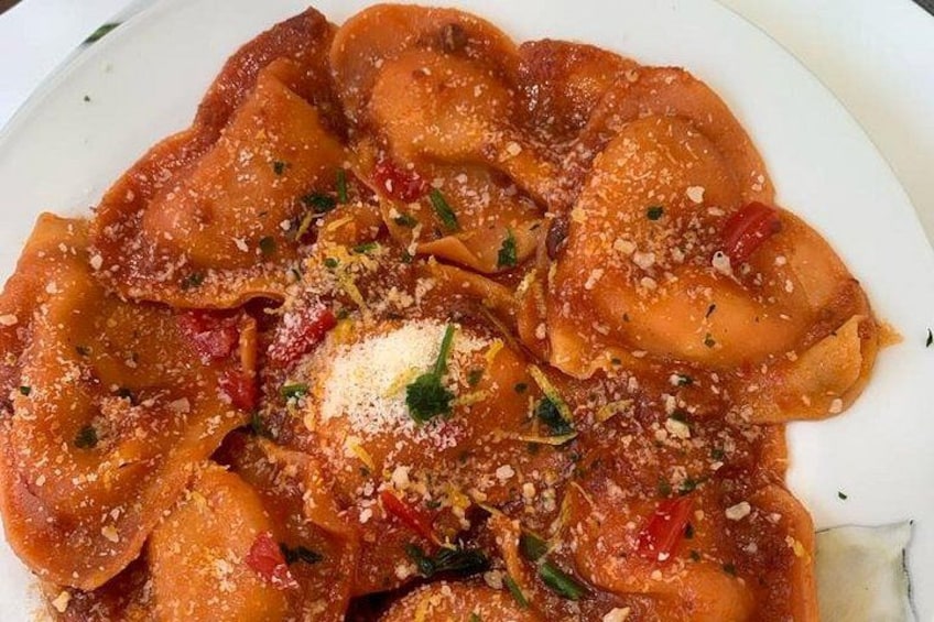 A plate of ravioli with tomato sauce, garnished with herbs and grated cheese. 1