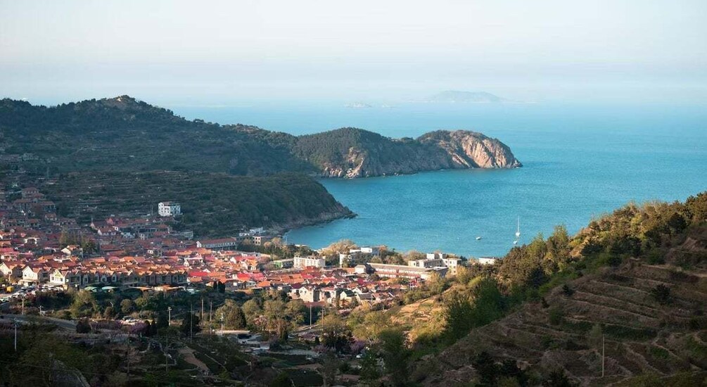 A coastal town with terraced fields, a harbor, and a mountainous backdrop. 1