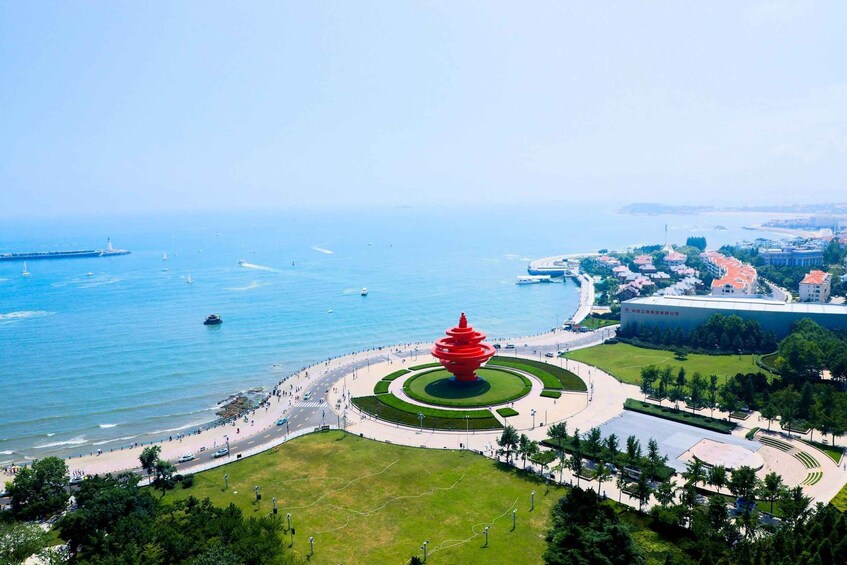 A coastal cityscape with a prominent red spiral sculpture, a waterfront promenade, and a large modern building. 4