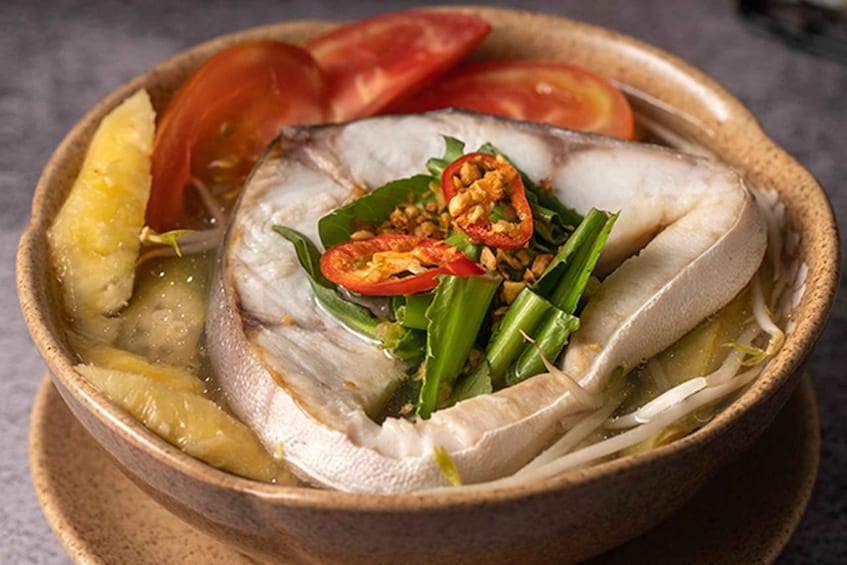 A bowl of fish soup with vegetables and herbs. 1