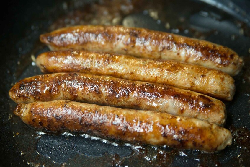 Four sausages cooking in a pan. 2