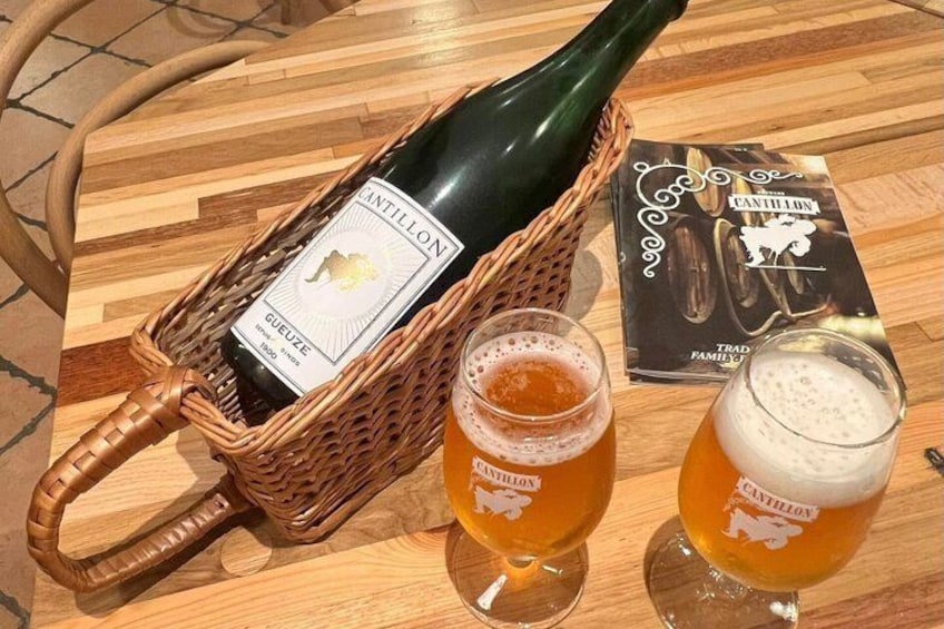 Een fles Cantillon wijn, twee bierglazen en een menukaart op een houten tafel. 3