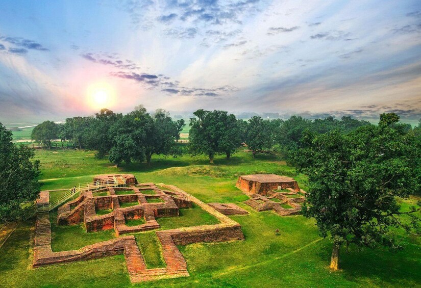 Ancient ruins with brick pathways and structures, surrounded by lush greenery and trees. 3