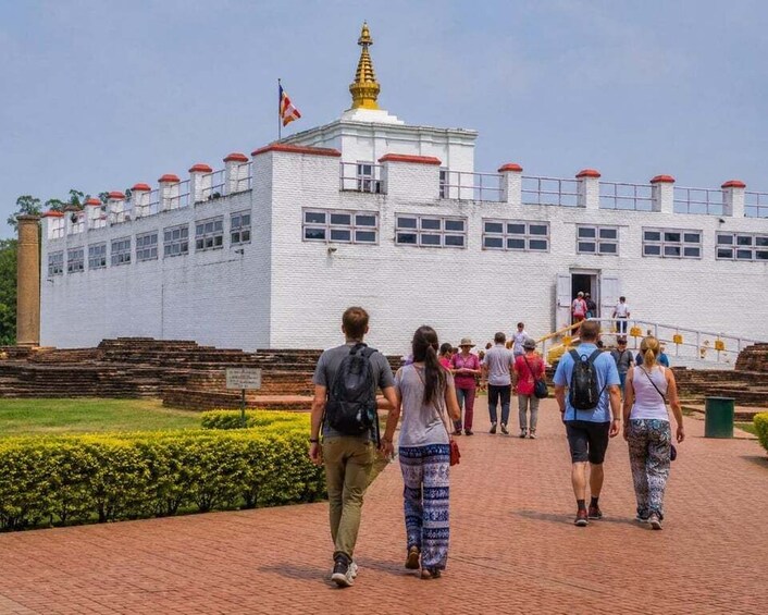 A white building with a golden spire, surrounded by tourists walking on a brick pathway. 1