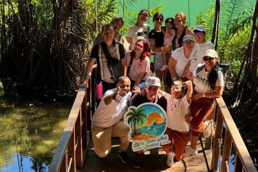 Un groupe de personnes se trouve sur un pont en bois, dans un cadre tropical caractérisé par une végétation luxuriante et une étendue d’eau. 2