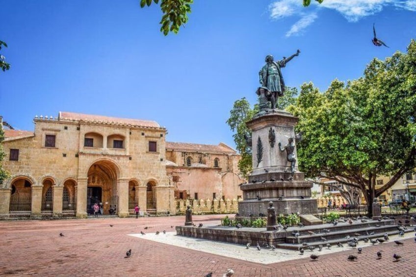 A historic building with arches, a statue, and a fountain in a plaza. 2