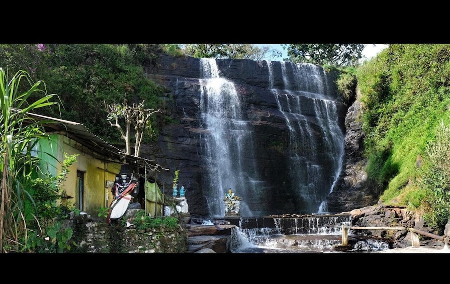 A waterfall cascading over a rocky cliff, surrounded by lush greenery and a small shrine with statues. 3