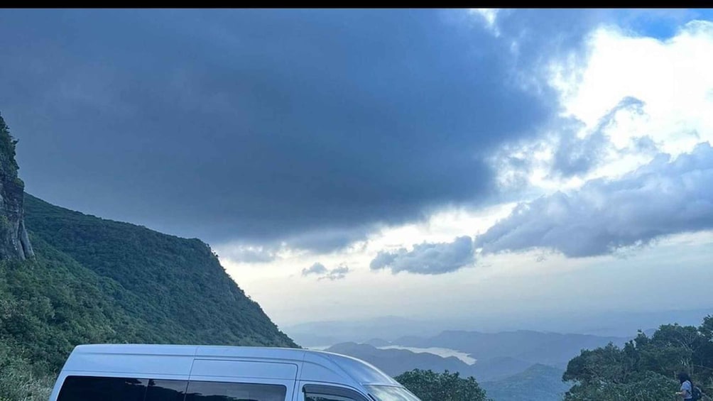 A white van parked on a mountain road with a cloudy sky above. 5