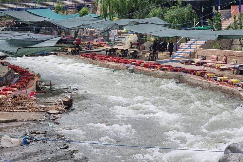A river with boats, a market area with tables and people, and a bridge in the background. 2